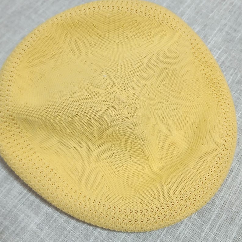 Puede incluir: Un gorro tipo boina de color amarillo p&aacute;lido hecho de tejido de punto. El sombrero tiene forma circular con una parte superior ligeramente puntiaguda y un borde decorativo perforado. La boina es de color amarillo claro s&oacute;lido.