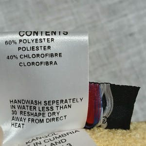 Puede incluir: Una etiqueta de tela blanca con texto negro que detalla el contenido y las instrucciones de cuidado. La etiqueta dice "CONTENTS" seguida de la composici&oacute;n de la tela: 60% poli&eacute;ster y 40% clorofibra. Las instrucciones de cuidado incluyen lavar a mano y evitar el calor directo.