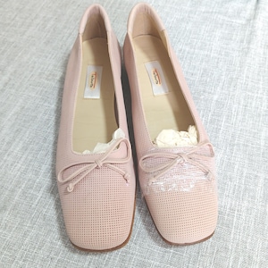 May include: A pair of light pink ballet flats with a perforated design. Each shoe features a small bow detail on the toe and a square toe. The brand name "Talbots" is visible on the insole of each shoe.