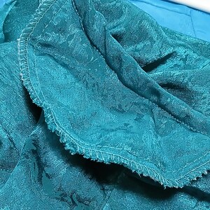 Peut inclure: Gros plan sur un tissu turquoise &agrave; motif floral. Le tissu est pli&eacute;, r&eacute;v&eacute;lant une surface textur&eacute;e et un bord cousu. La couleur est un turquoise vif, avec de subtiles variations de tons.