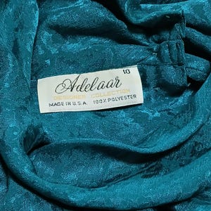 Peut inclure: Gros plan sur un tissu de couleur teal avec un motif floral. Une &eacute;tiquette blanche indique "Adelaar DESIGNER COLLECTION MADE IN U.S.A. 100% POLYESTER". L'&eacute;tiquette porte &eacute;galement le num&eacute;ro "10".