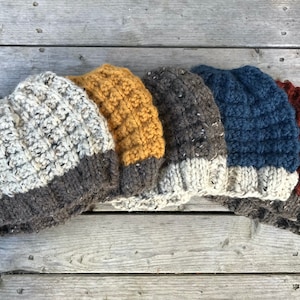 May include: Five knitted hats in different colors, including gray, yellow, brown, blue, and red. The hats are all made with a textured stitch and have a folded brim.