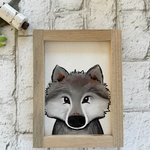 May include: A framed illustration of a wolf's face. The wolf is drawn in a cartoon style with a gray and brown fur pattern. The frame is made of light wood.