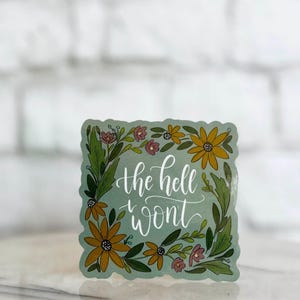 May include: A teal blue sticker with a floral border and the text "the hell won't" in white cursive lettering.