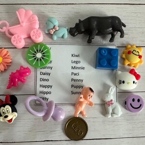 May include: Assortment of colorful plastic toys, including a pink baby carriage, a black hippo, a blue Lego block, a pink pacifier, a pink and white bunny, a pink and white Hello Kitty, a yellow sun, a purple smiley face, a pink dinosaur, a green kiwi, a pink daisy, a pink and white Minnie Mouse, a pink and white puppy, a pink and white baby doll, and a pink and white kitty.