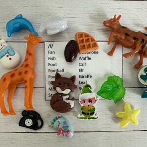 May include: A collection of colorful plastic figurines, including a giraffe, a snowman, a fish, a calf, an elf, a fox, a leaf, a starfish, a waffle, a phone, a fan, and a football. The figurines are arranged on a wooden surface.