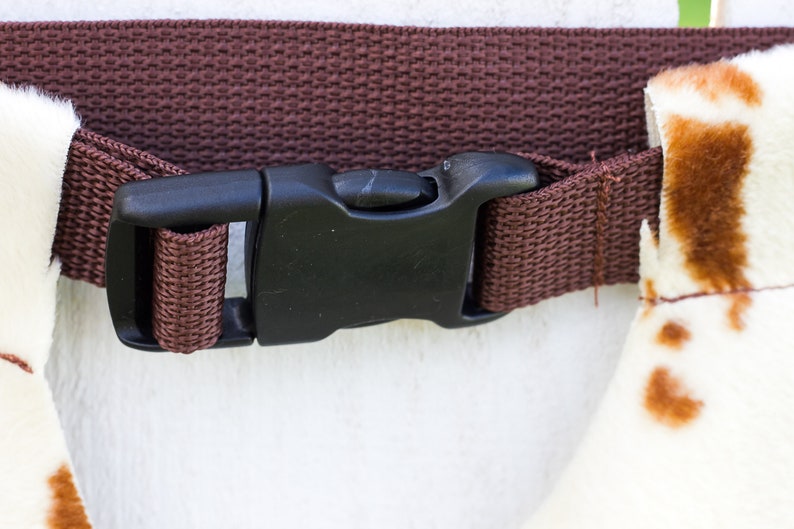 May include: A brown adjustable strap with a black plastic buckle. The strap is made of woven fabric.
