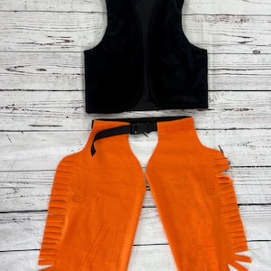 May include: A black sleeveless vest paired with bright orange chaps. The vest features a simple open front design. The orange chaps have a black adjustable belt with a plastic buckle closure and decorative fringe detailing along the outer edges.