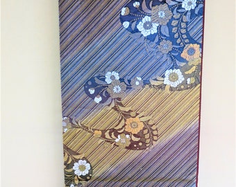 May include: A decorative textile with a diagonal striped pattern in shades of gold, blue, and purple. The design features stylized floral motifs in white, brown, and orange. The edges are finished with a burgundy border.