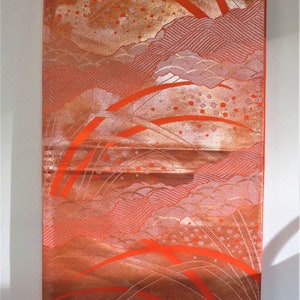 May include: A vertical textile with a Japanese-inspired design. The fabric features a blend of orange, red, and gold hues, with stylized mountain and cloud motifs. The design includes curved lines and small, scattered details.