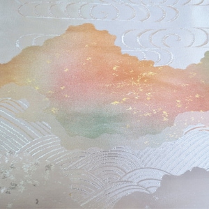 May include: A close-up of a textile with a cloud-like design. The fabric features a gradient of colors, including peach, orange, and green, with gold flecks. White, swirling patterns create a sense of depth and movement.