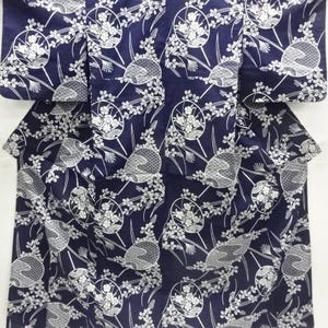 May include: A navy blue Japanese yukata with a white floral and fan pattern. The fabric is folded, showing the collar and the upper part of the garment. The design features circular floral motifs and fan-shaped elements.