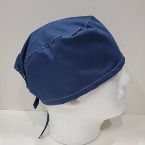 May include: A navy blue surgical scrub cap with white stitching along the seams. The cap is tied at the back with two fabric ties. The cap is displayed on a white mannequin head.
