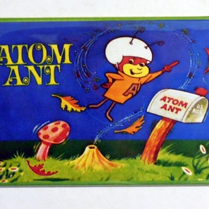 May include: A vintage Atom Ant magnet featuring a cartoon ant wearing a helmet and flying through the air. The magnet has a blue background with stars and leaves. The text "ATOM ANT" is written in yellow letters at the top of the magnet.