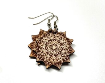 May include: A pair of brown wooden earrings with a white mandala design. The earrings have silver hooks.