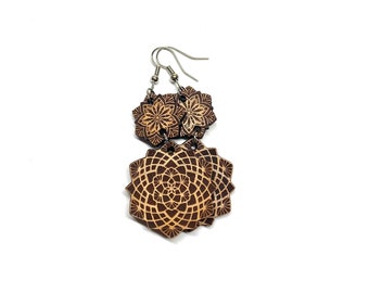 May include: A pair of wooden earrings with a geometric design. The earrings are brown with a light brown mandala pattern. The earrings are attached to silver hooks.