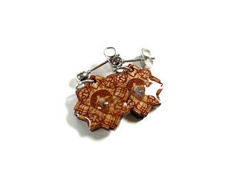 May include: A pair of wooden earrings with a star-shaped design and a silver post. The earrings are brown and have a clear resin coating.