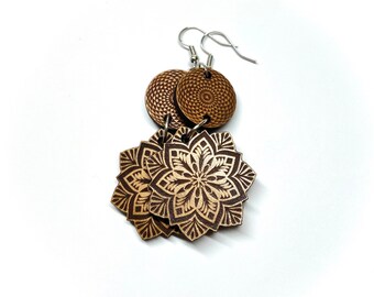May include: A pair of wooden earrings with a mandala design. The earrings are brown with gold accents and have a circular shape.