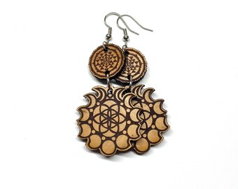 May include: A pair of wooden earrings with a geometric design. The earrings are brown and gold in color and feature a circle with a flower of life pattern inside. The earrings are hanging from silver hooks.