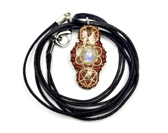 May include: A brown and gold pendant with a moonstone in the center, hanging from a black cord. The pendant features a geometric design.