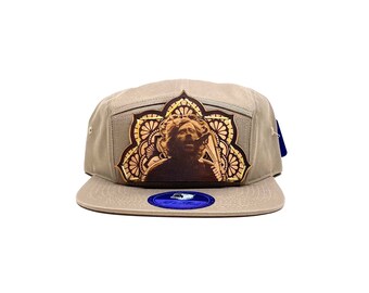 May include: A tan canvas 5-panel hat with a brown leather patch featuring a mandala design and a portrait of a person. The patch is attached to the front of the hat.