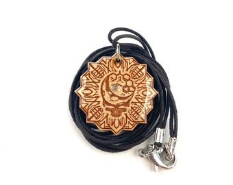 May include: A wooden pendant with a geometric design and a crescent moon with a small crystal in the center. The pendant is on a black cord with a silver clasp.