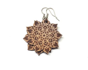 May include: A pair of brown leather earrings with a mandala design. The earrings are made of two layers of leather, with the top layer being a lighter shade of brown than the bottom layer.