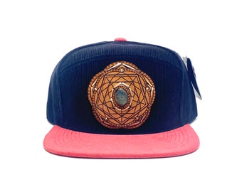 May include: A black corduroy baseball cap with a red brim and a gold geometric design with a blue stone in the center.