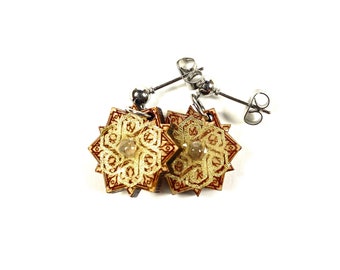 May include: A pair of gold and brown star-shaped earrings with a clear stone in the center. The earrings are made of wood and have a silver post.