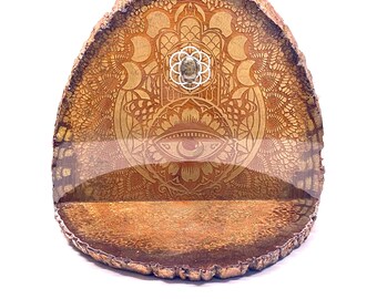 May include: A wooden shelf with a carved mandala design, featuring a hamsa hand and an eye symbol. The shelf is made from a natural tree slice and has a rustic, earthy look.