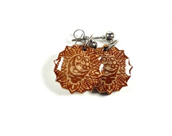 May include: A pair of brown and silver earrings with a mandala design. The earrings are made of wood and have a silver post.