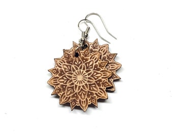 May include: A pair of brown wooden earrings with a mandala design. The earrings are made of wood and have a silver hook.