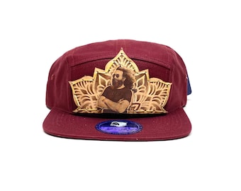 May include: A maroon 5-panel baseball cap with a brown leather patch featuring a portrait of Jerry Garcia and a mandala design.