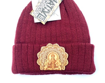 May include: A maroon beanie with a wooden patch featuring a golden deity figure surrounded by a mandala design. The beanie has a tag attached that reads "NATIVE ELEMENT".