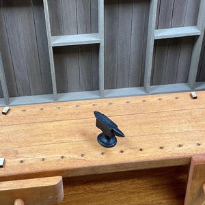 May include: A miniature wooden workbench with a small black metal anvil on top. The workbench has a drawer and a small wooden vise on the side.