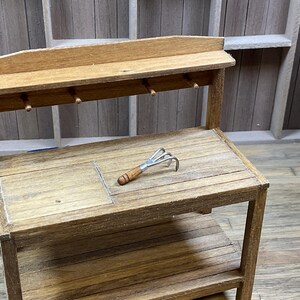 May include: A wooden workbench with a shelf and a small hand rake on the top surface.