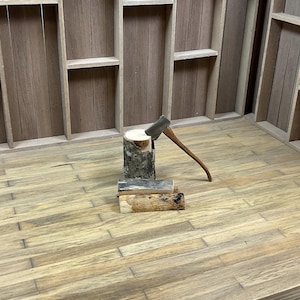 May include: A miniature wooden log cabin with a small axe and a pile of logs in front of it. The cabin has a wooden roof and walls, and the logs are stacked neatly.