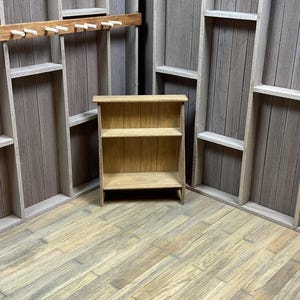 May include: A small wooden shelf with two shelves. The shelf is made of unfinished wood and has a rustic look. The shelf is sitting on a wooden floor.