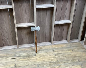 May include: A wooden-handled sledgehammer with a silver head, leaning against a wooden wall with shelves.