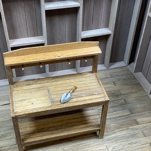 May include: A wooden workbench with a shelf and a small metal shovel on top. The workbench is in a room with wooden walls and a wooden floor.