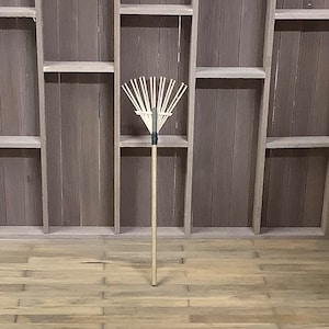 May include: A wooden rake with a long handle, standing upright against a wooden shelf unit.