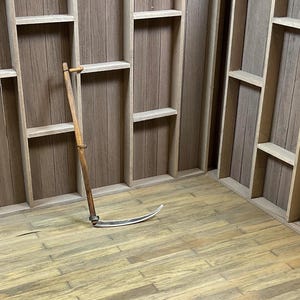 May include: A wooden wall with shelves, a wooden floor, and a metal scythe leaning against the wall.