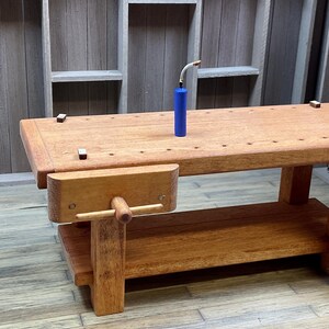 May include: A wooden workbench with a vise and a blue propane tank. The workbench has a wooden top and a lower shelf. The workbench is in a workshop setting.