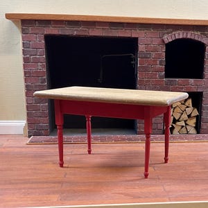 May include: A small red table with a light wood top. The table has four legs and is in front of a brick fireplace.