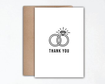 May include: A white card with a black line drawing of two interlocked rings with a diamond on top. The text "THANK YOU" is printed below the rings.