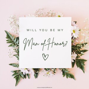 Pode incluir: Um cart&atilde;o branco com o texto "Voc&ecirc; quer ser meu padrinho?" escrito em fonte de caligrafia preta com um pequeno cora&ccedil;&atilde;o desenhado abaixo do texto. O cart&atilde;o est&aacute; rodeado de flores brancas e rosas sobre um fundo rosa claro.
