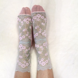May include: A pair of sheer pink socks with a delicate floral lace pattern in shades of pink and blue.