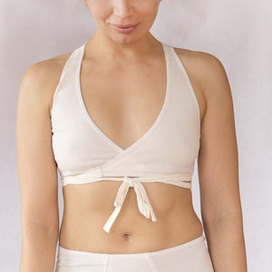 May include: A white wrap-style bralette with adjustable straps. The bralette is made of a soft, stretchy fabric and has a deep V-neckline.