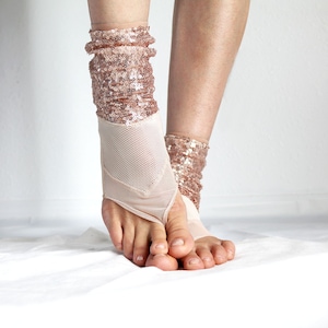 May include: A pair of rose gold sequined socks with a mesh design. The socks are worn on a person's feet.