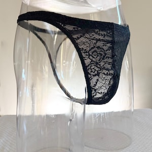 Puede incluir: Braga de encaje negro con un diseño floral, exhibida en un maniquí transparente. La delicada tela de encaje revela el intrincado patrón y la textura de la prenda.